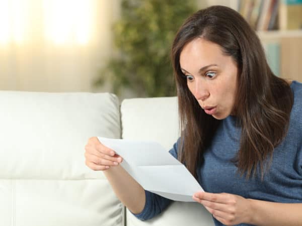 Surprised woman reading a letter on a couch at home