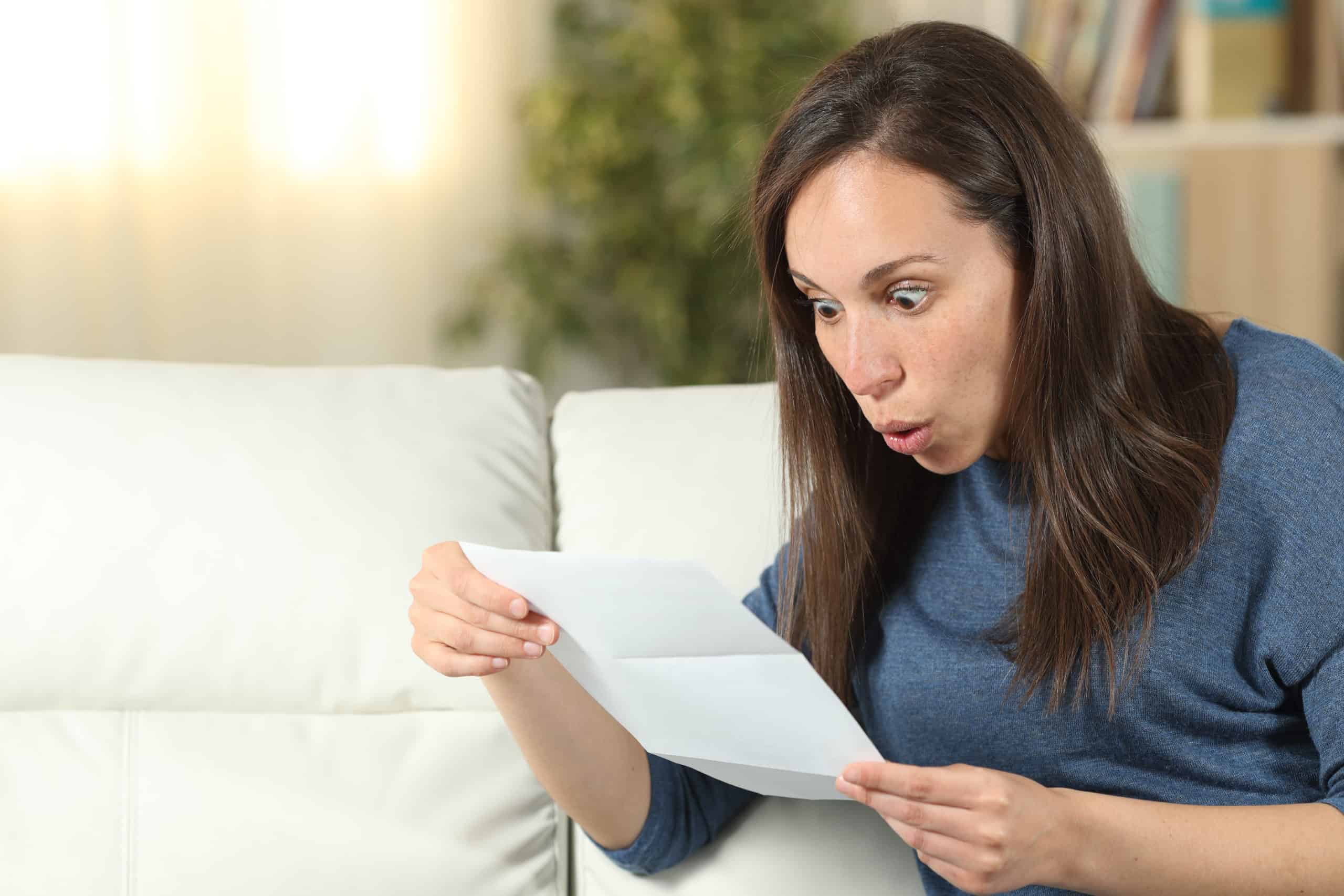 Surprised woman reading a letter on a couch at home