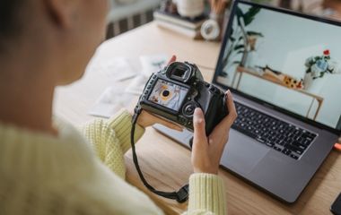 This photo of of a photographer looking at a photo on their camera infront of their laptop, the photo is to show the importance of social media photography.