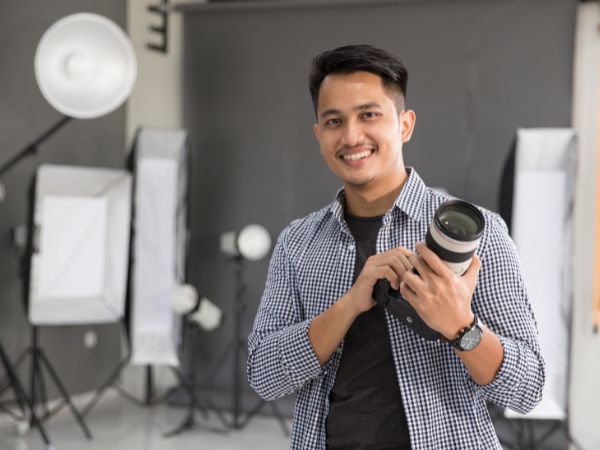 A confident male photographer holding a telephoto lens in a studio setup, highlighting professionalism.