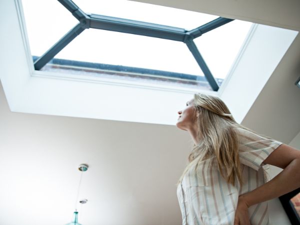 Woman looking up at a skylight with natural light streaming through, planning her photoshoot.