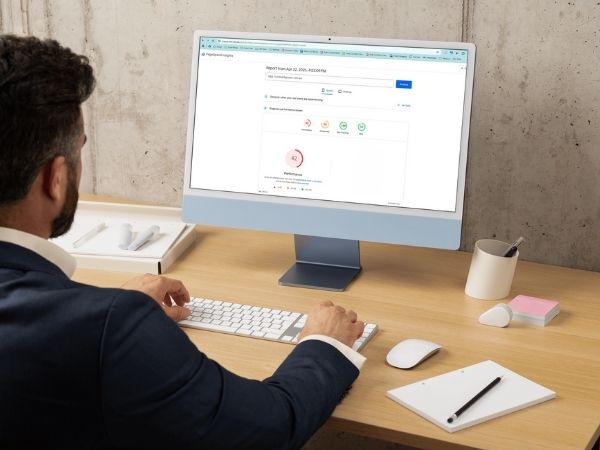 Man in a suit sitting at a desk viewing a website performance report on a desktop screen, analysing page speed and security indicators for a medical website.
