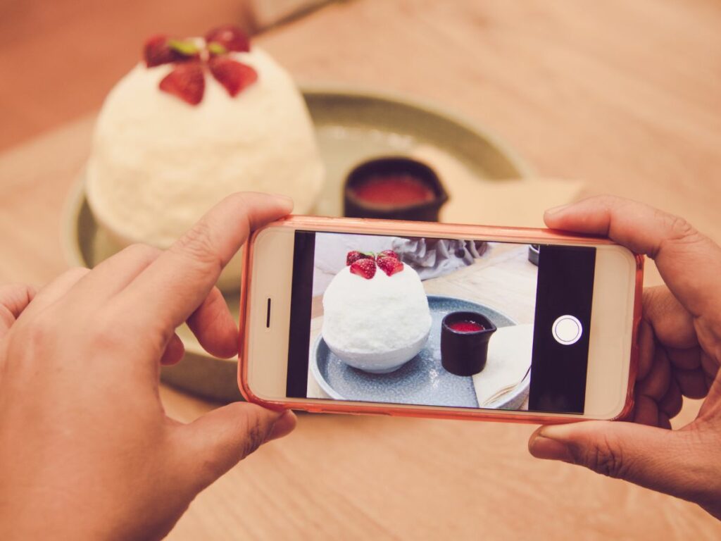 Close-up of a person taking a photo of a dessert topped with strawberries using a smartphone, representing user-generated content in action.