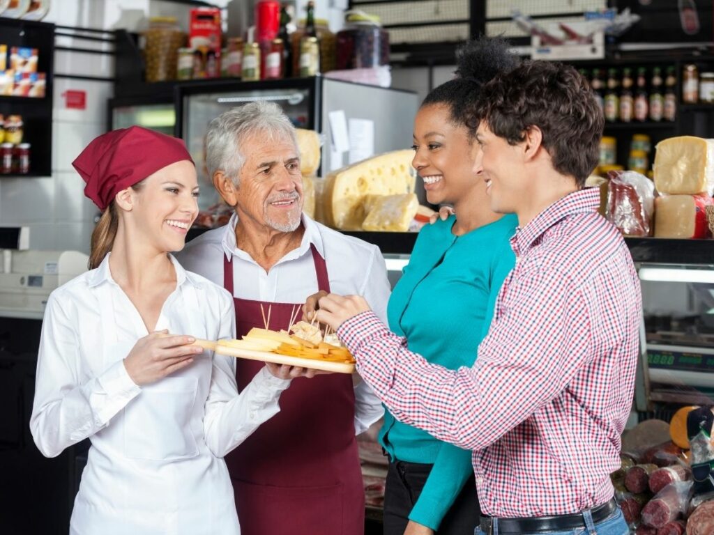 Cheese shop staff interacting with smiling customers while offering samples, symbolising community engagement and word-of-mouth content.