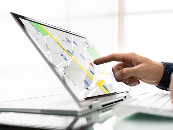 Finger pointing to a map on a laptop with red location pins, representing local business visibility and search intent.