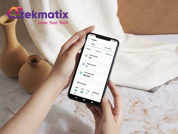 Hands holding a smartphone showing the Tekmatix mobile dashboard with metrics and insights. Tekmatix logo with tagline “Love Your Tech” in the corner.