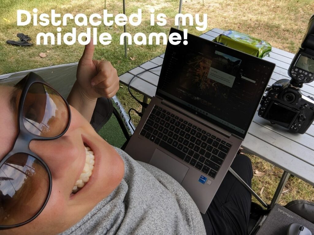 Ellie Clare working outdoors with a laptop and camera gear, highlighting the real-life challenges of staying focused with ADHD. - Image text says; "Distracted is my middle name!"