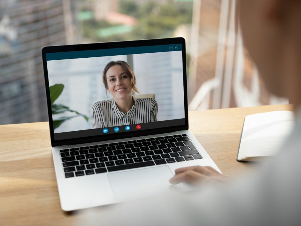 Professional woman smiling during a Zoom meeting on a laptop, demonstrating good online meeting etiquette with natural light and a tidy background