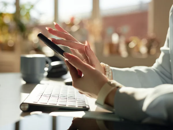A business owner typing on a smartphone beside a computer keyboard in bright natural light, symbolising digital engagement and online communication for modern businesses in 2025. A business owner typing on a smartphone beside a computer keyboard in bright natural light, symbolising digital engagement and online communication for modern businesses in 2025.
