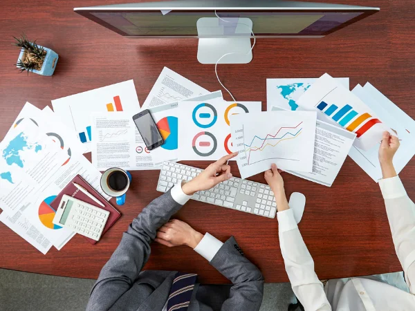Two professionals analysing printed marketing and SEO reports at a desk covered with charts and graphs, illustrating the performance gap between digitally active and offline small businesses in Western Australia. Two professionals analysing printed marketing and SEO reports at a desk covered with charts and graphs, illustrating the performance gap between digitally active and offline small businesses in Western Australia.