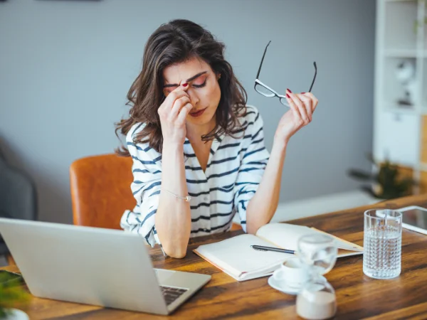 A woman at a desk with a laptop, holding her glasses and rubbing her eyes in frustration, showing the stress of relying solely on social media for business marketing. A woman at a desk with a laptop, holding her glasses and rubbing her eyes in frustration, showing the stress of relying solely on social media for business marketing.